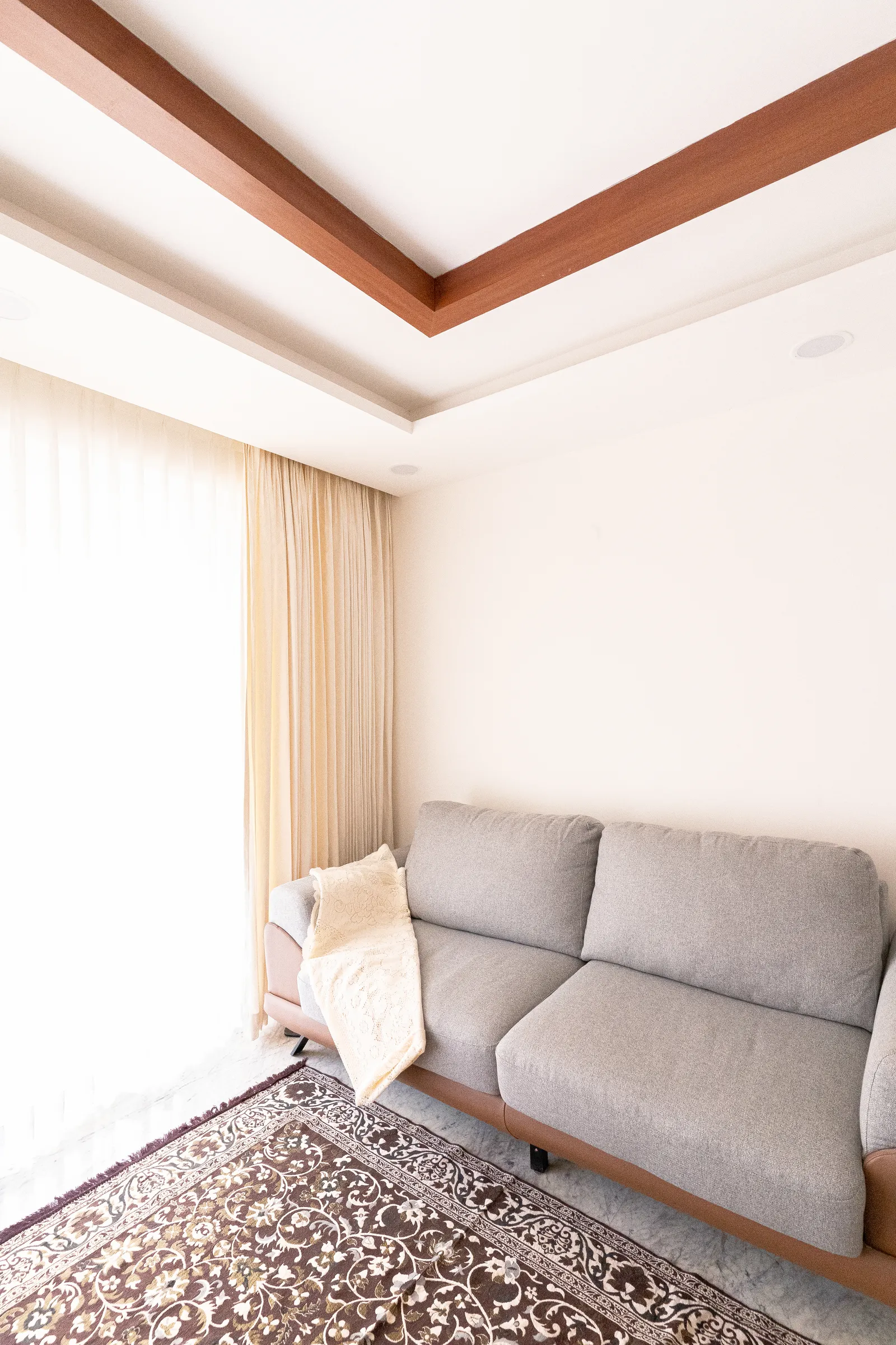 Grey sofa beneath a timber-trimmed false ceiling — Karthik's Residence